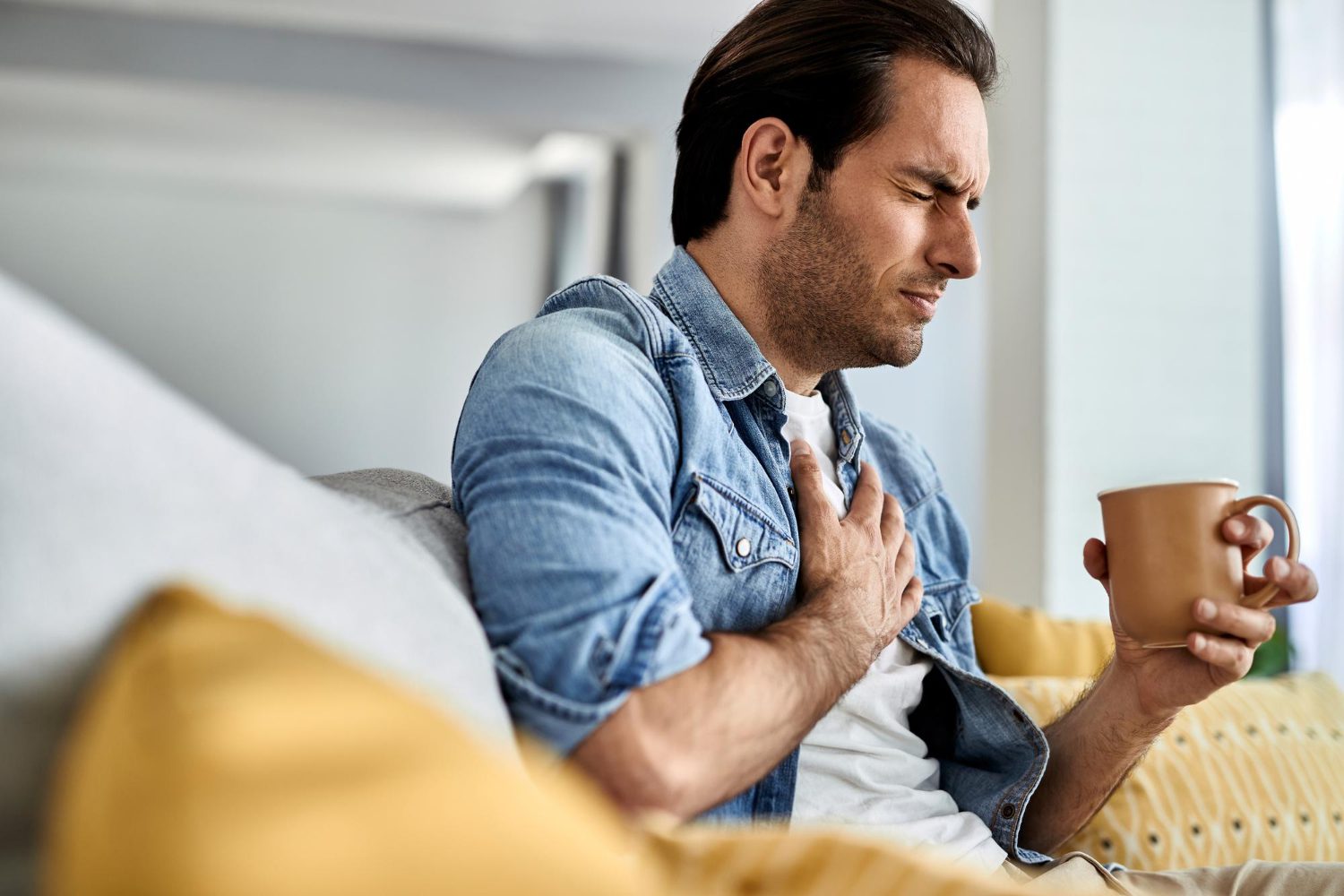 young-man-feeling-sick-holding-his-chest-pain-while-drinking-tea-living-room